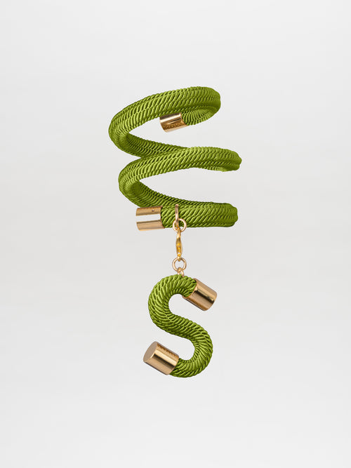 Introducing the Nicky Bracelet Green by Tcherassi, a stunning piece that gracefully forms an "S" shape with its gold accents against its green background, reminiscent of a delicate keychain crafted from gold-plated brass.