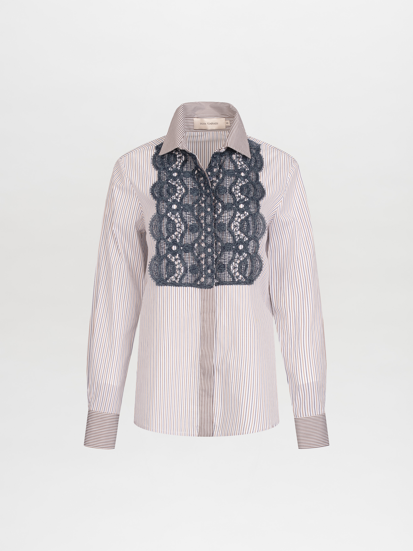 A person with blonde hair slicked back wears a white shirt with vertical stripes and a detailed blue lace front, along with textured blue pants and a belt with large pearl-like embellishments. Now available for pre-order, the Naroa Shirt Blue Brown Stripes will ship by 2024.