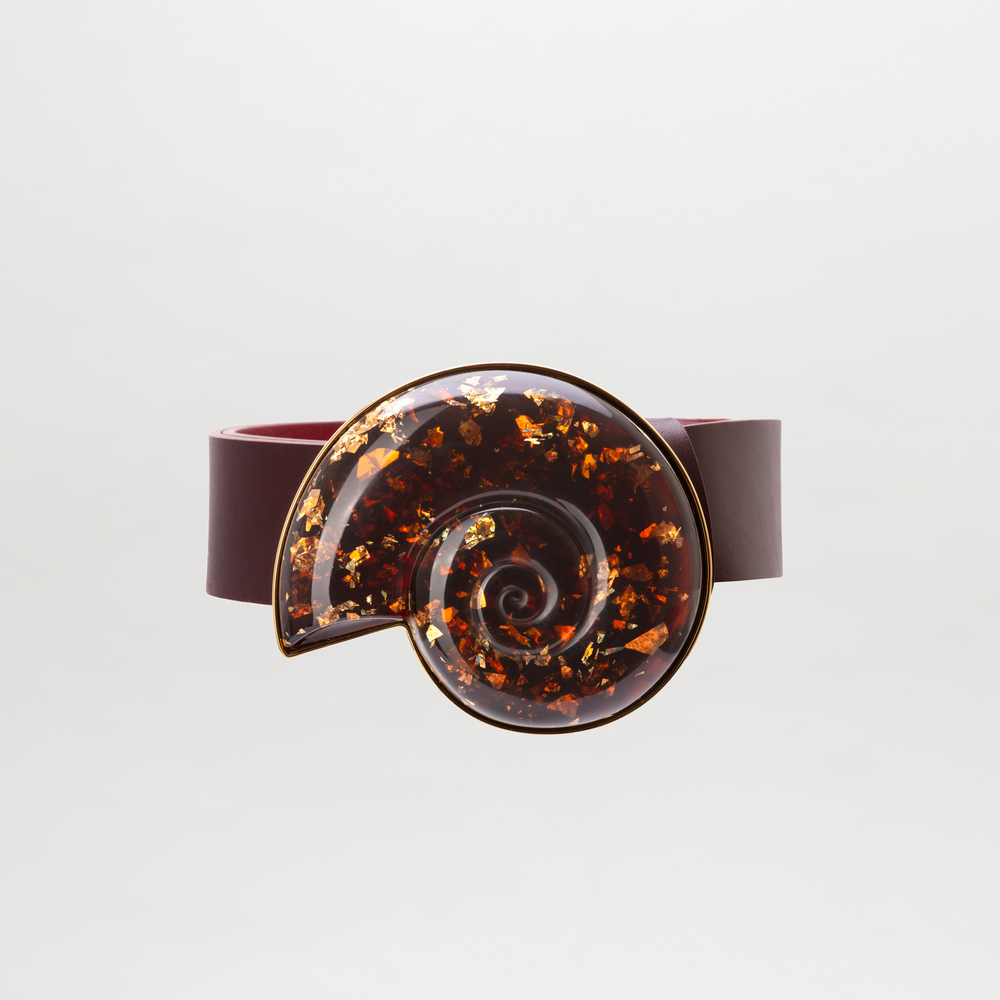 The Nautilus Belt is a dark red Italian leather belt with a large, glossy Petralux Fantasy Stone spiral buckle with gold flecks, shown on a plain white background.