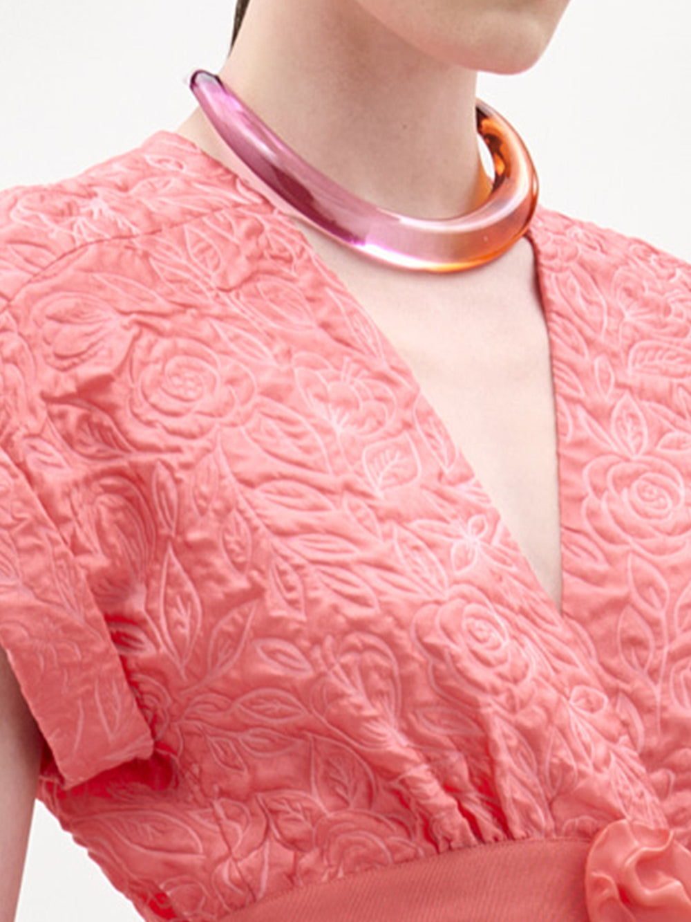 Close-up of a person wearing a pink textured dress with a large pink necklace.