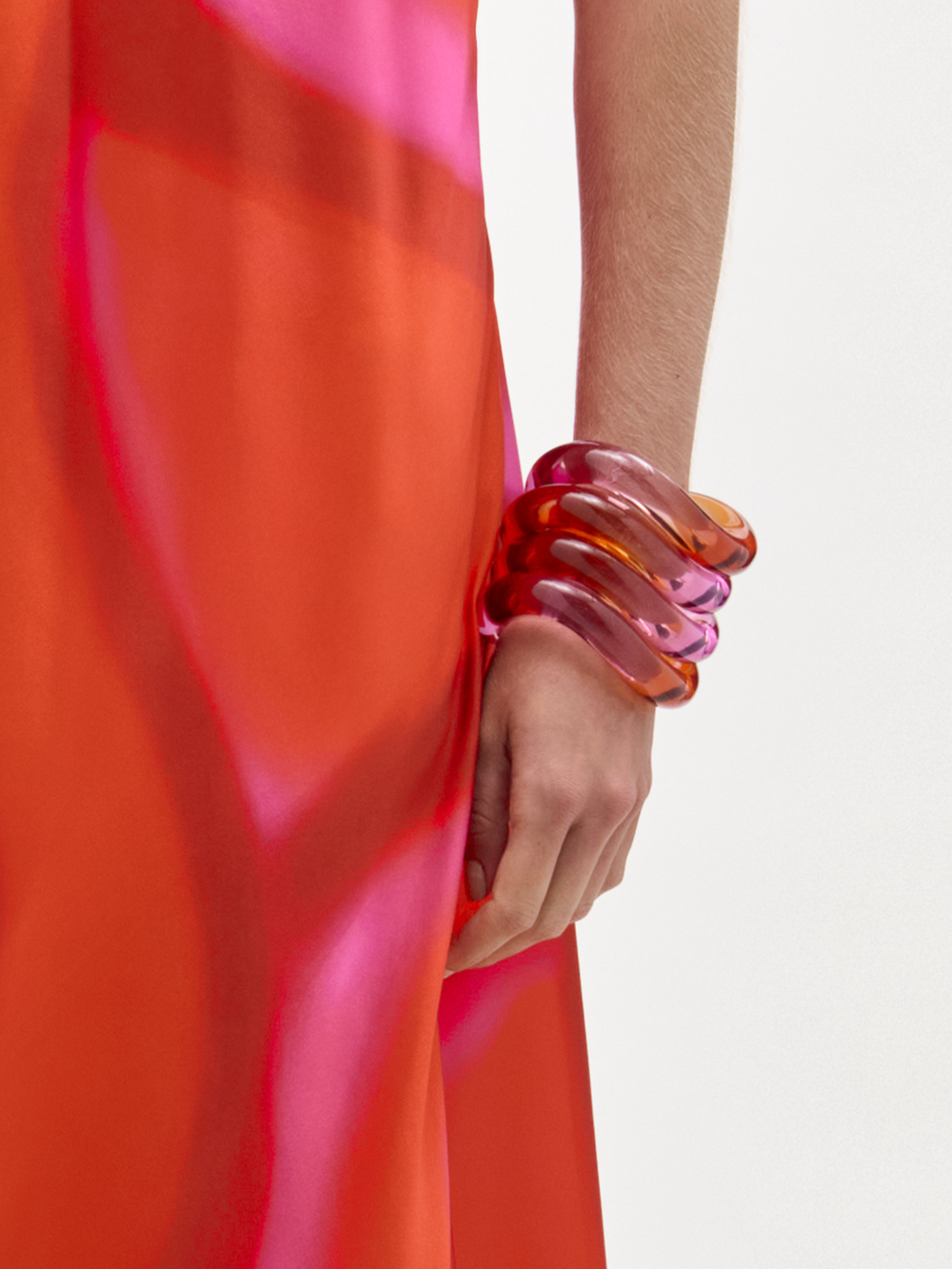 Person wearing a bright red garment with a hand adorned with colorful bangles on a light background