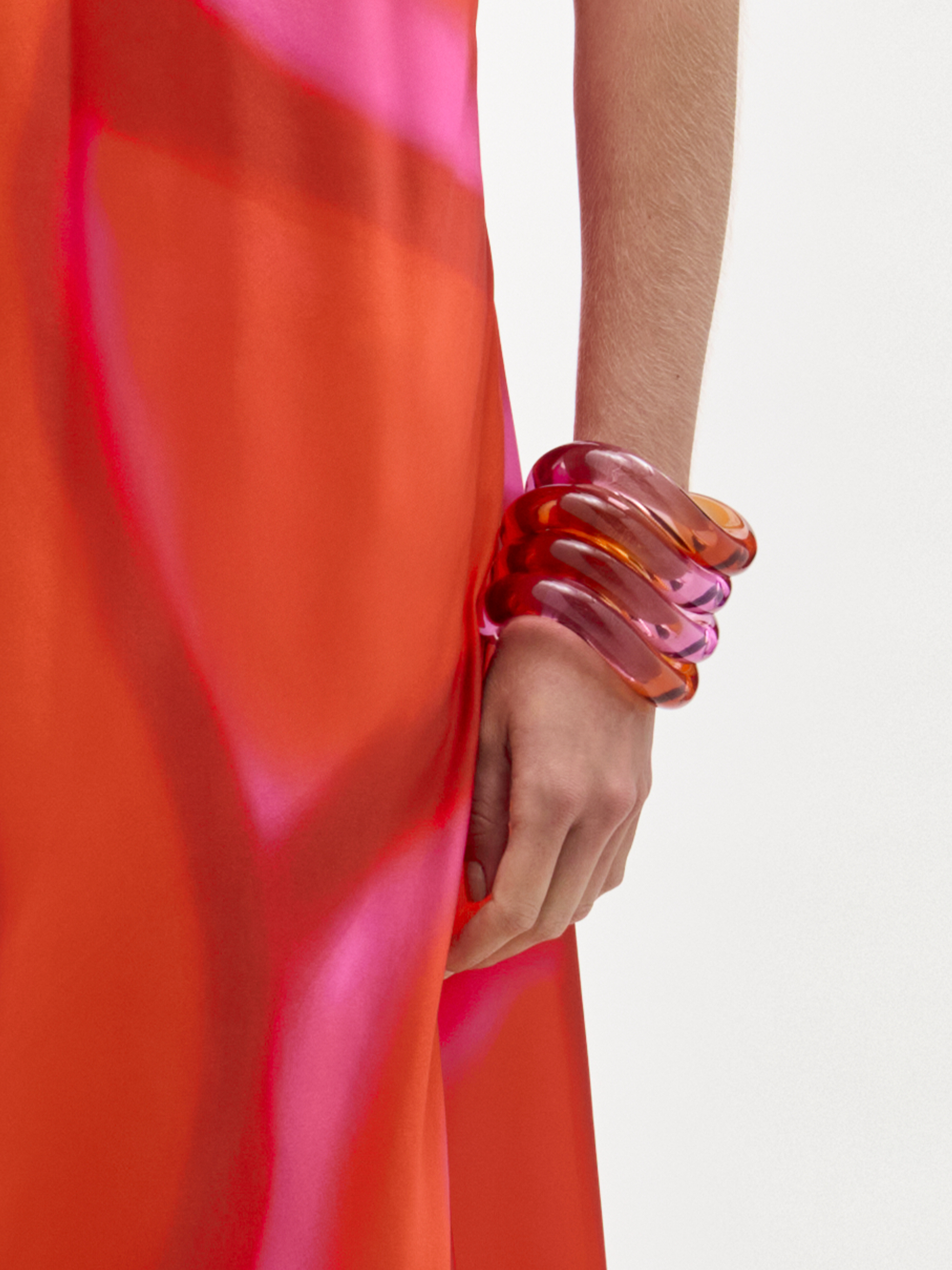 Person wearing a bright red garment with a hand adorned with colorful bangles on a light background
