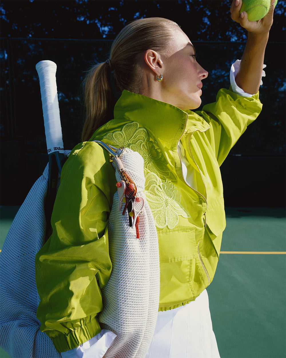 Person in a bright green jacket holding a tennis ball on a tennis court