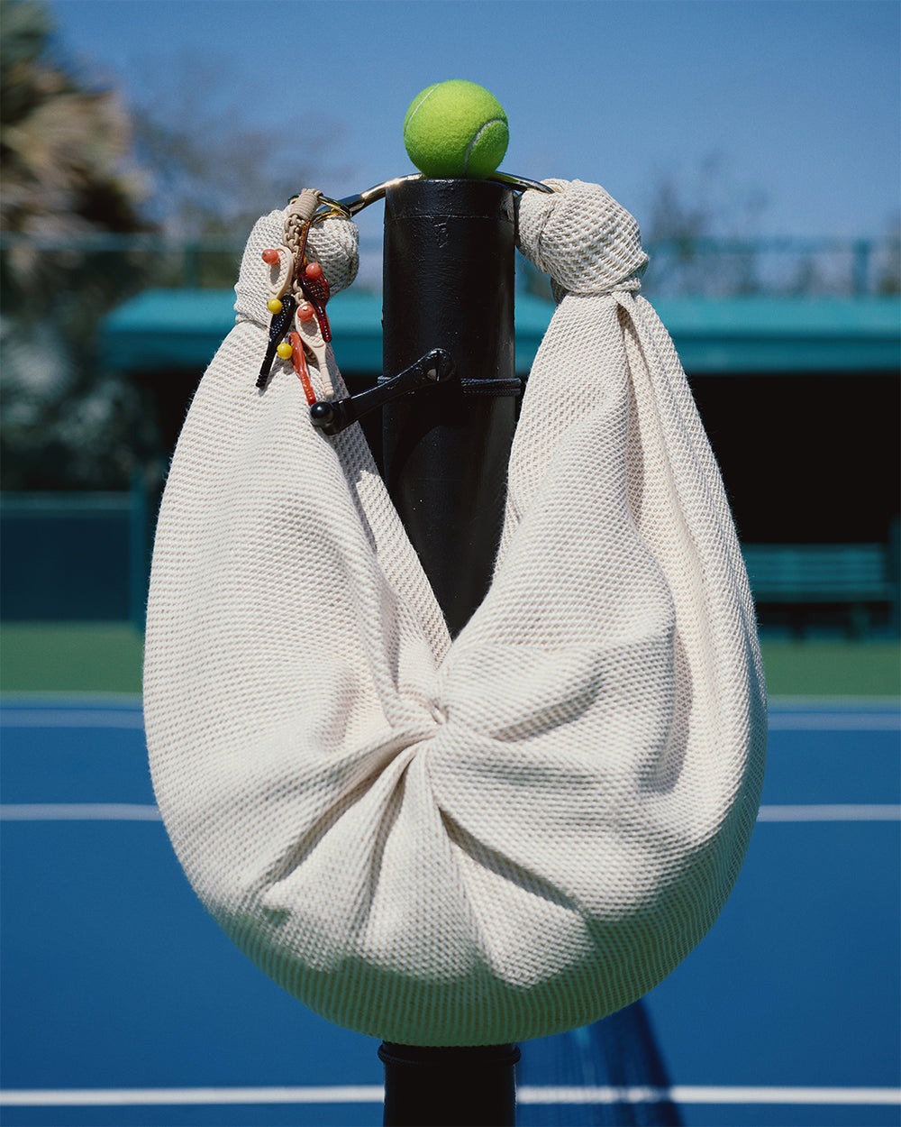 White bag with a tennis ball on top against a blurred tennis court background