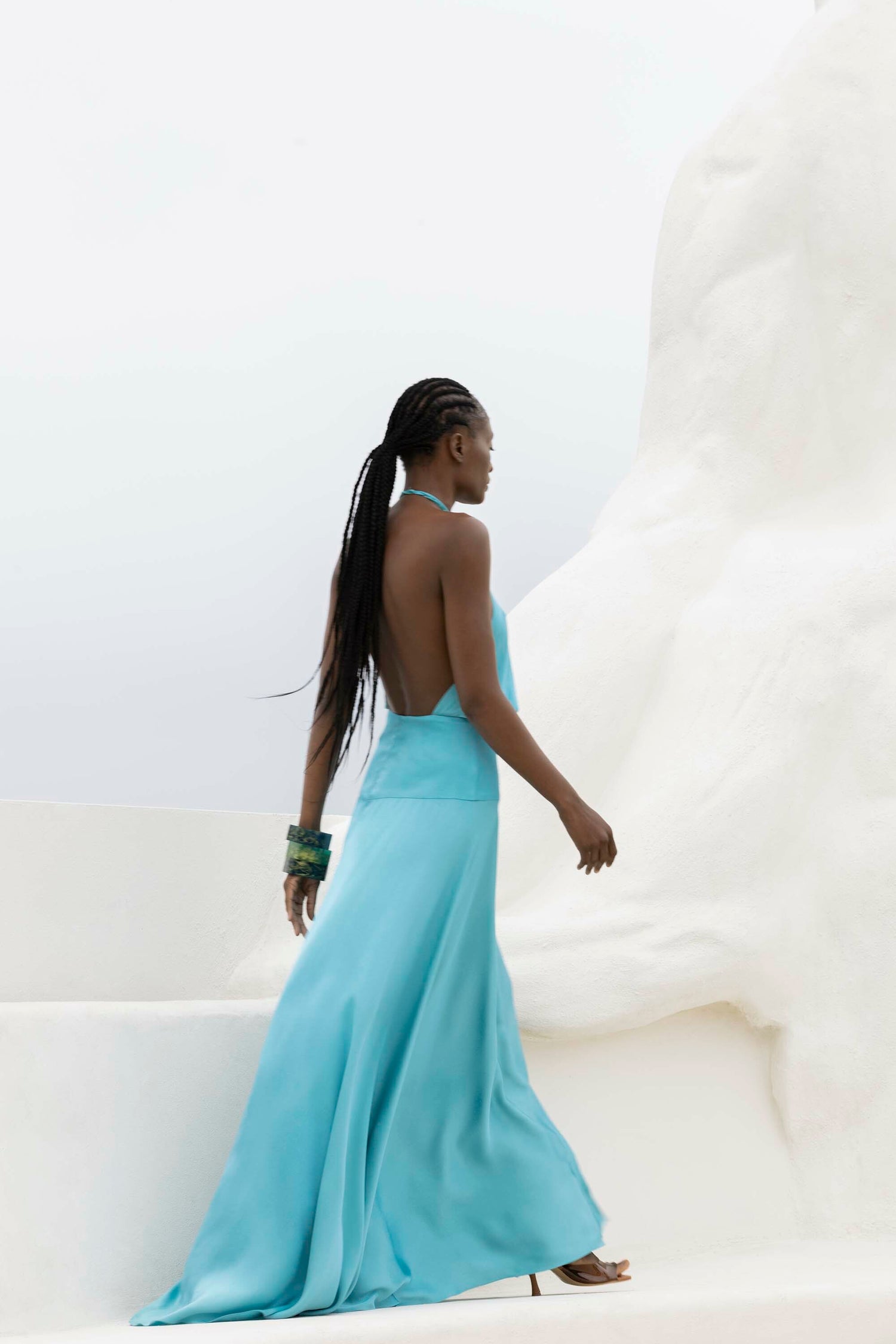 A woman in a blue backless gown walks up white steps next to a large abstract sculpture.