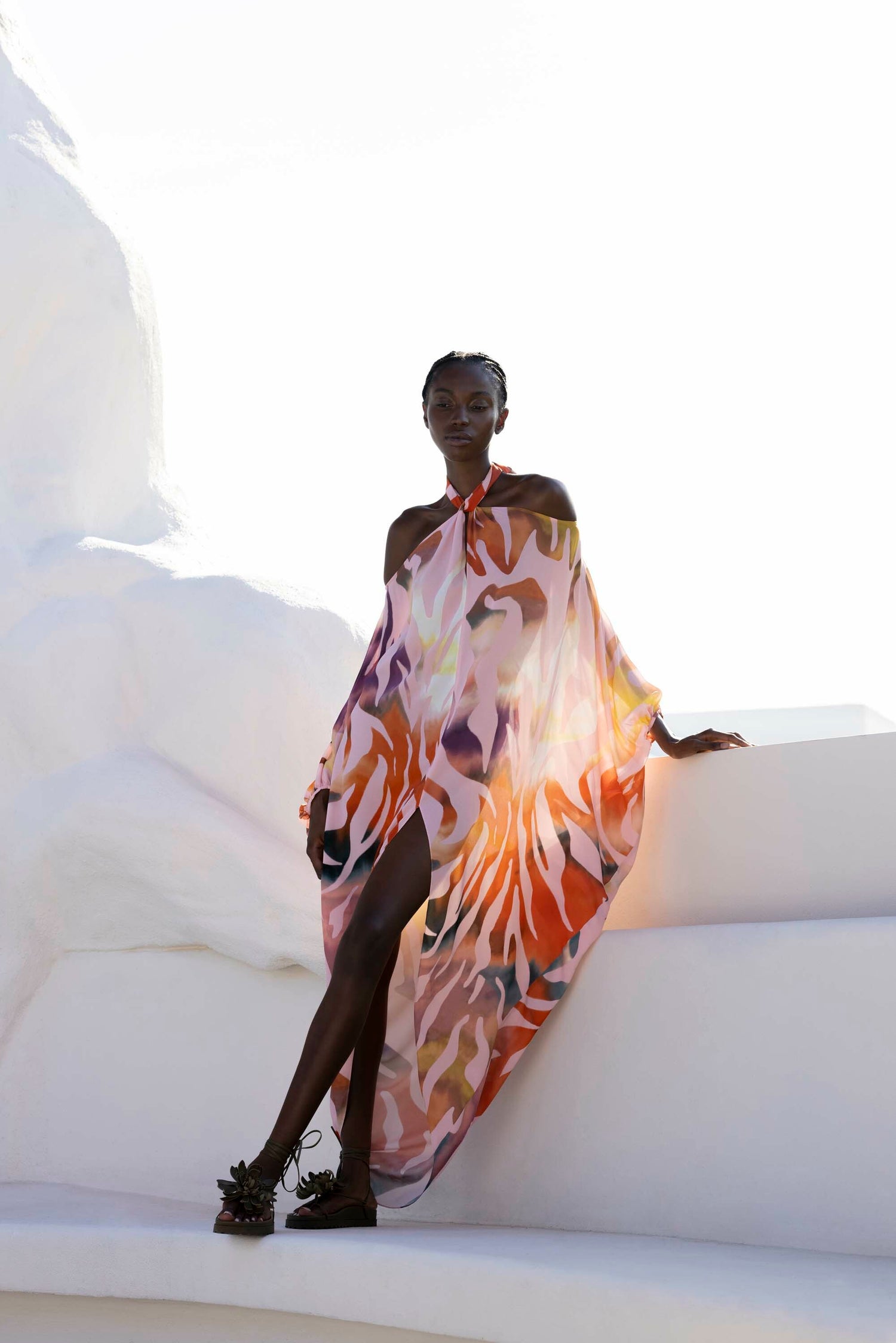 Person in a colorful, flowing dress sits on white steps with one leg crossed, holding a phone.