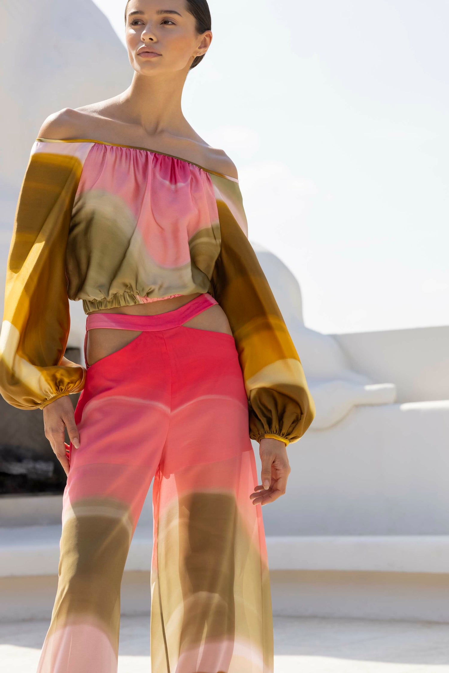 A person wearing a colorful off-the-shoulder blouse and matching wide-leg pants stands outdoors against a bright sky.