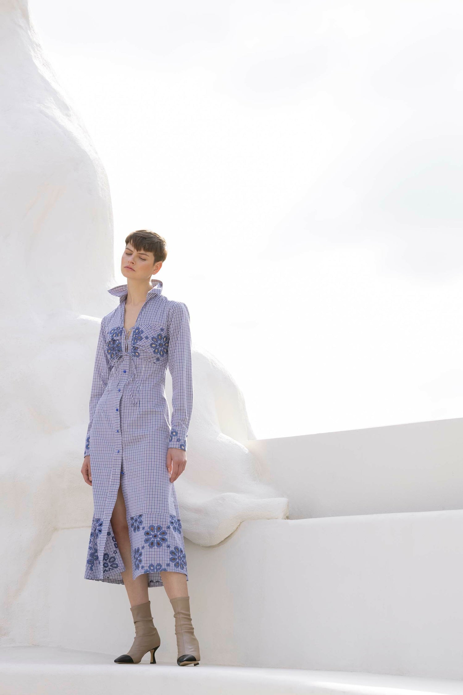 Person wearing a blue and white patterned dress stands on white steps with a clear sky background.