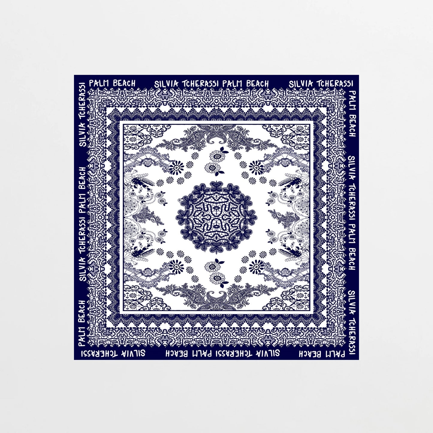 The Palm Beach Scarf is a square silk scarf featuring blue floral and geometric patterns on white, inspired by Mediterranean lace. Its blue border displays "PALM BEACH SILVIA TCHERASSI" in white lettering.