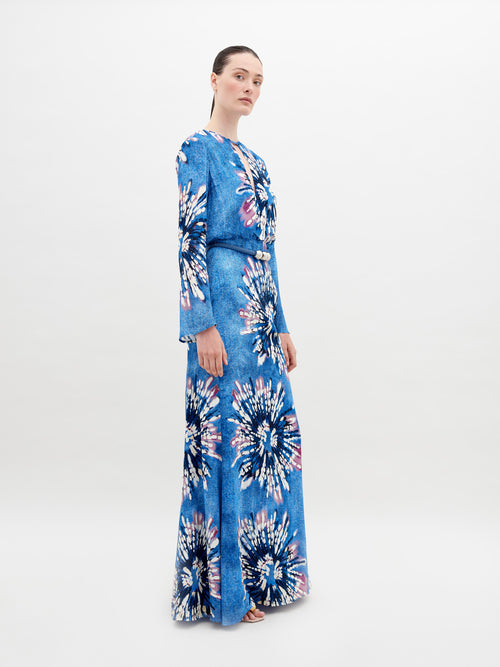 A person stands wearing the Ravenna Dress Aciano Flower, looking off to the side against a plain white background. Pre-order now to ensure it arrives by November 15th, 2024.