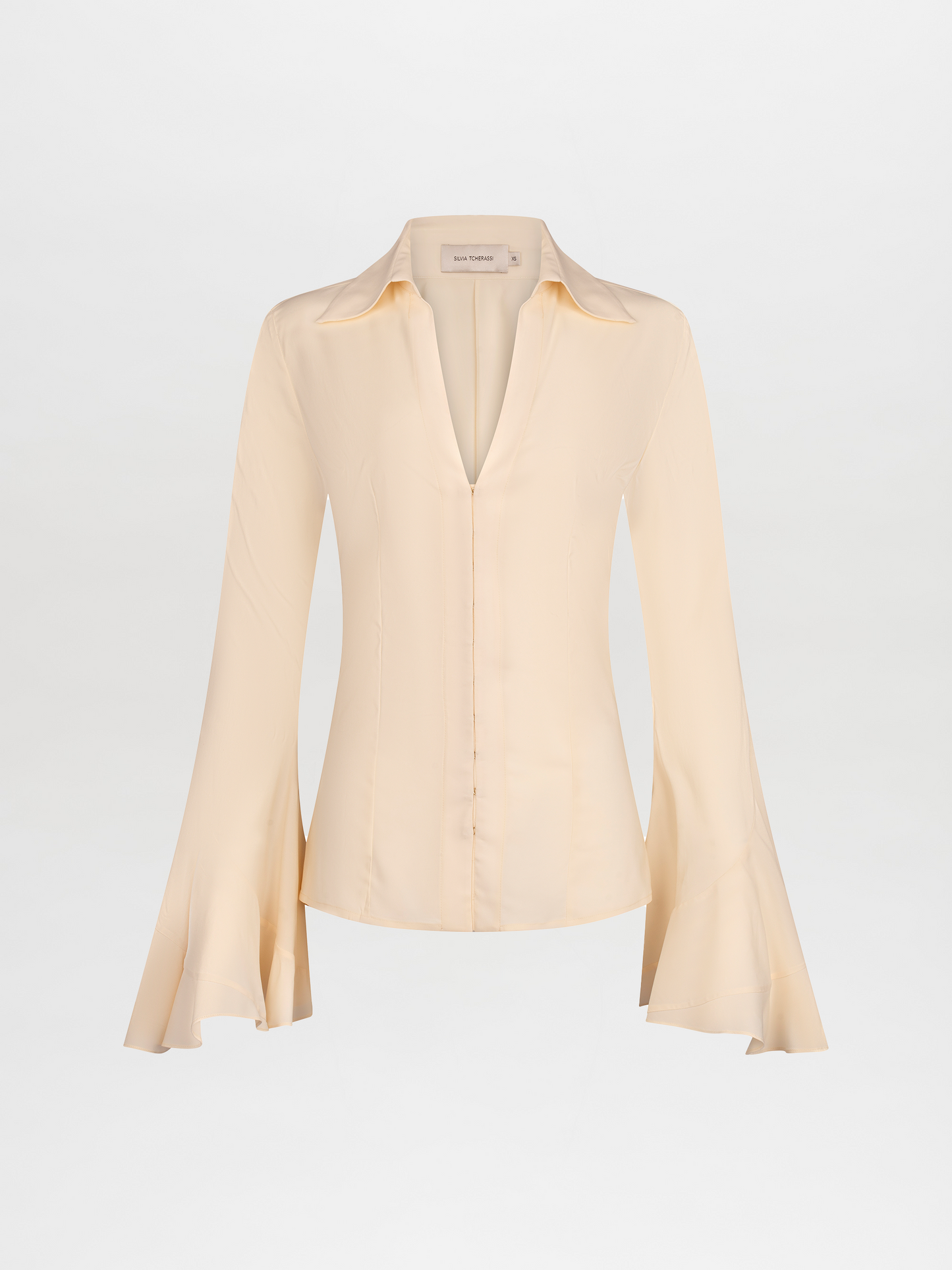 A long-sleeve, cream-colored Reggie Blouse Vanilla with flared cuffs and a V-neckline is displayed against a plain white background. Available for pre-order now, it will ship November 2024.