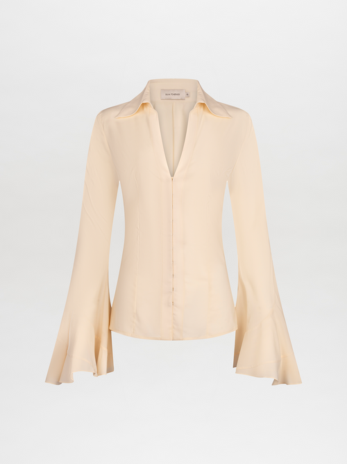 A long-sleeve, cream-colored Reggie Blouse Vanilla with flared cuffs and a V-neckline is displayed against a plain white background. Available for pre-order now, it will ship November 2024.