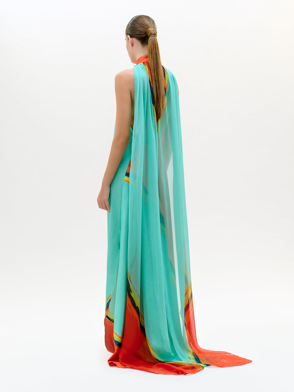 Woman wearing a long, light blue dress with colorful patterns on a white background