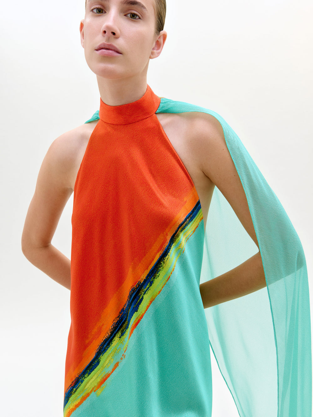 Model wearing a vibrant orange and teal dress with a colorful stripe on a white background