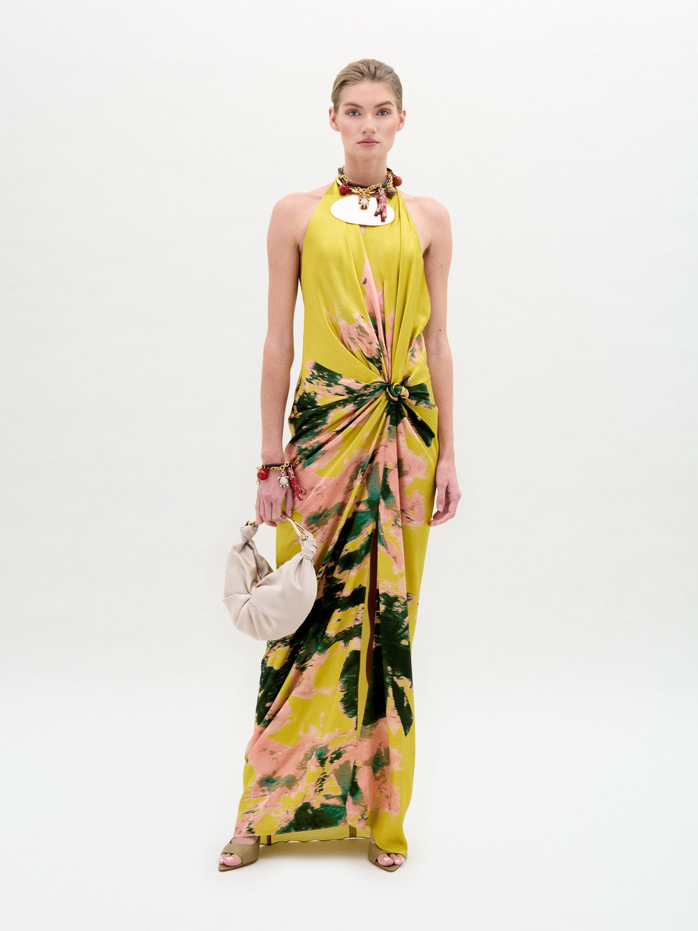 A person in the Sabrina Dress, a yellow and pink tie-dye style with a knotted front, holds a cream bag against a plain background.