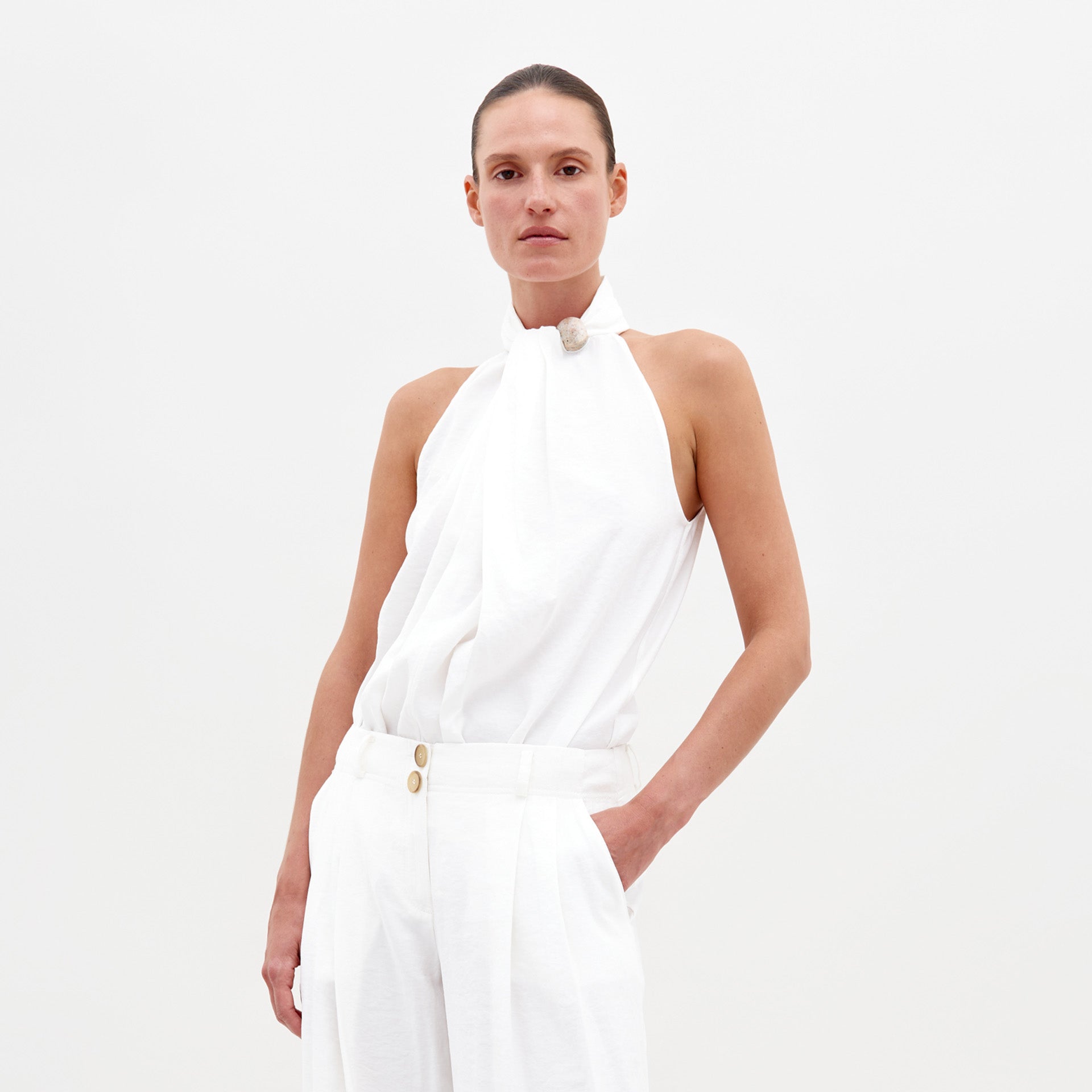 Person wearing the Shela Blouse White and white pants, standing against a plain white background. Ship by date: February 15th, 2025.