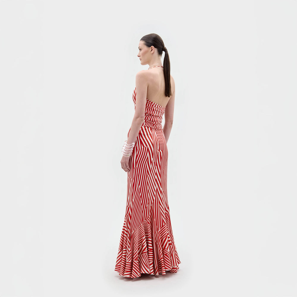 A woman stands against a plain white background wearing the Florina Skirt, a floor-length, red and white striped piece with a fitted waist and mermaid silhouette, crafted from luxurious Italian fabric.