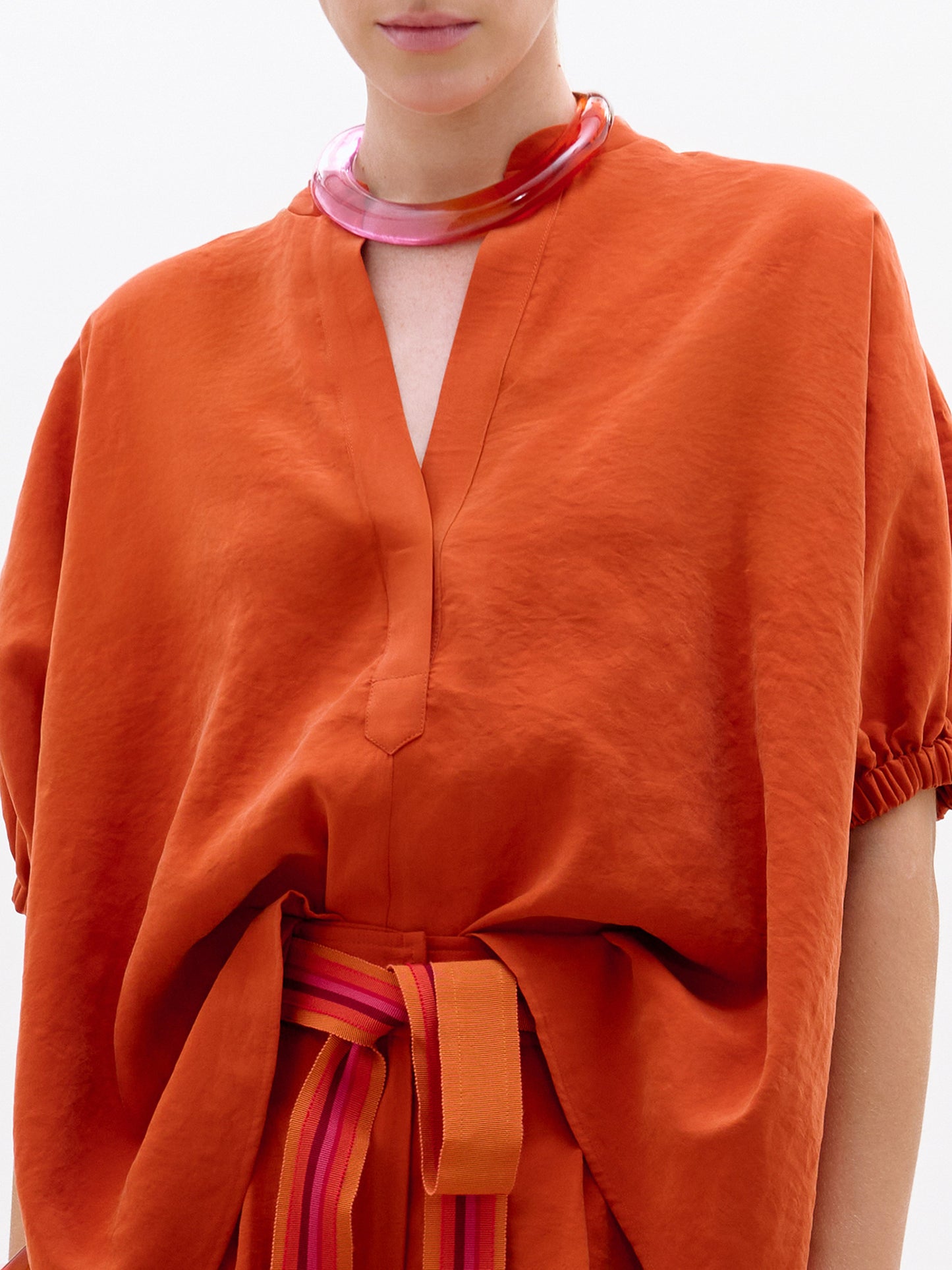 Orange outfit with a belt and pink necklace on a white background