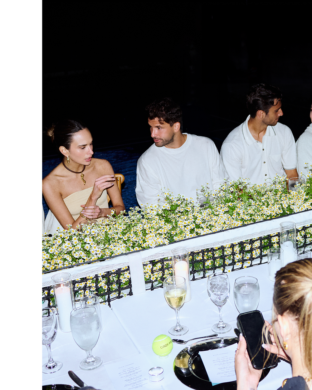 People sitting at a dinner table with floral arrangements and wine glasses.