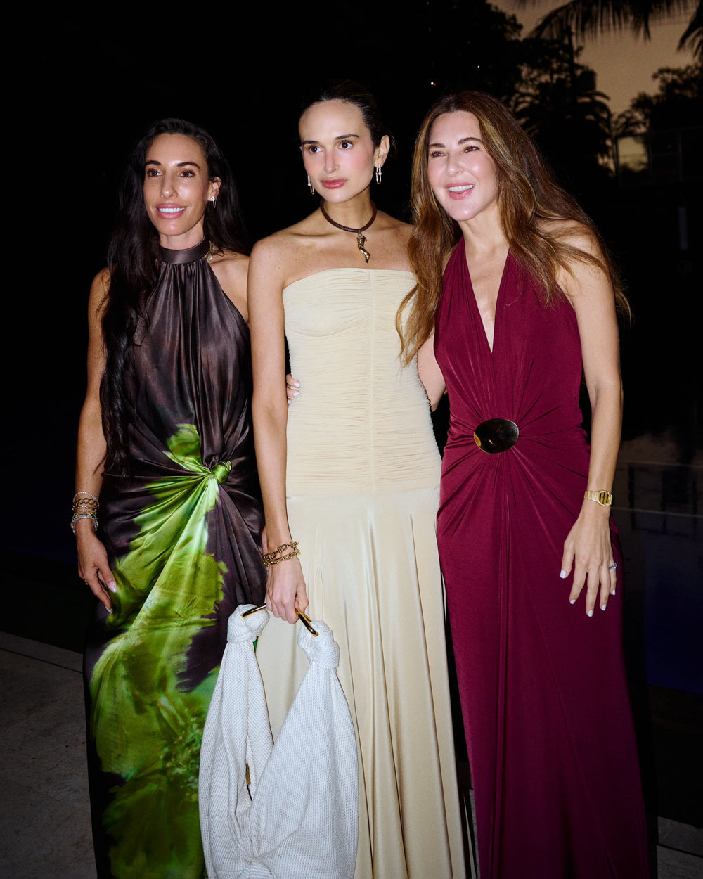 Three women in formal dresses standing together at an event.