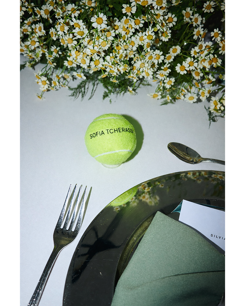 Green tennis ball with branding on a table setting with flowers and cutlery.