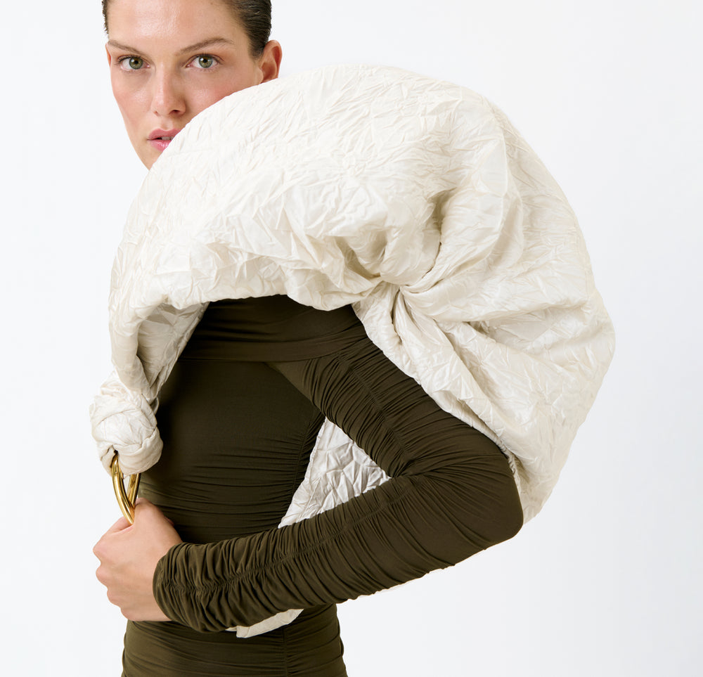 A person wearing a fitted olive-green outfit holds the Sofia Bag (Maxi), a large, textured off-white Italian fabric bag, draped over one shoulder against a plain white background.
