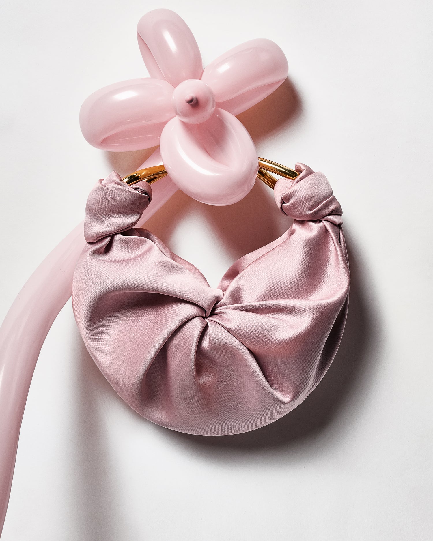 Pink satin handbag with balloon-like accessories on a white background