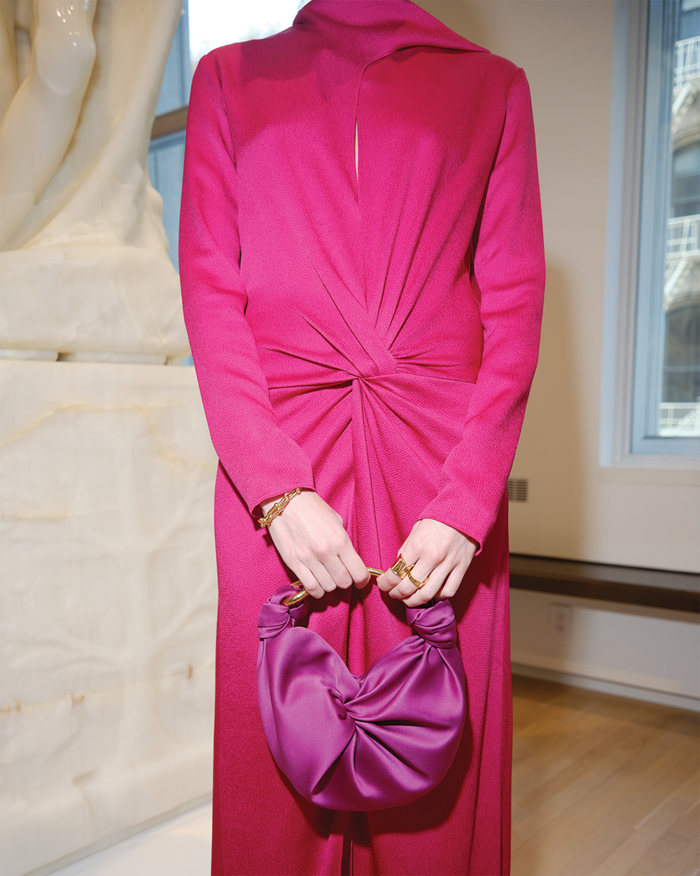Person wearing a bright pink dress holding a matching handbag indoors.