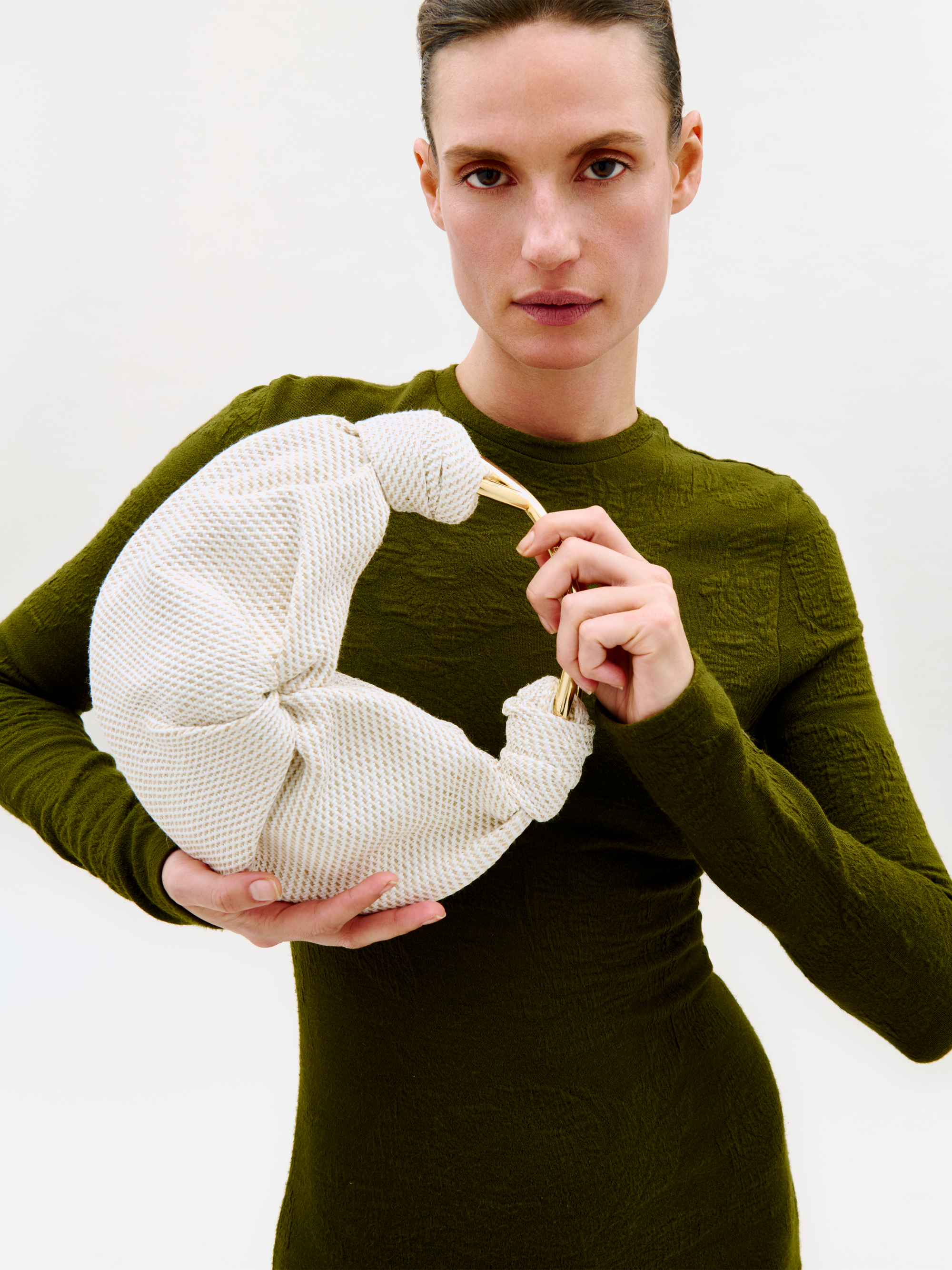 Woman holding a white knitted bag against a plain background
