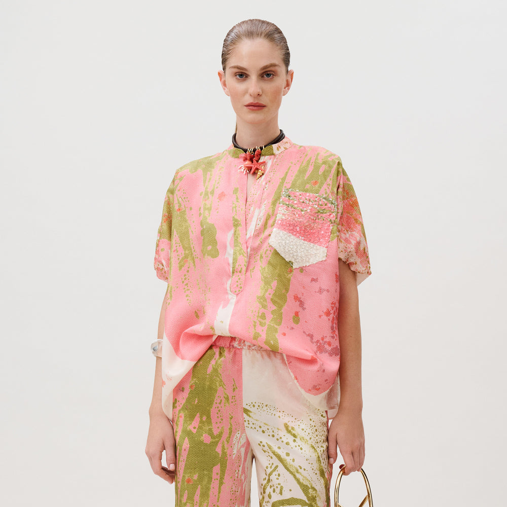 A model wears the Susane Blouse, a short-sleeved silk top paired with matching trousers featuring an abstract pink and olive green design, made in Colombia.
