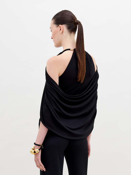 A person with tied-back hair wears a Tabatha Blouse Black with gold accents and a matching gold bracelet, standing against a plain white background. This stylish ensemble is available for pre-order now, with a ship by date of November 15th, 2024.