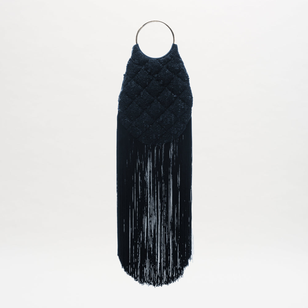 The Toblach Bag is a black, textured Jacquard bag featuring a quilted pattern, metallic top handles, and long black fringe at the bottom, shown against a white background.