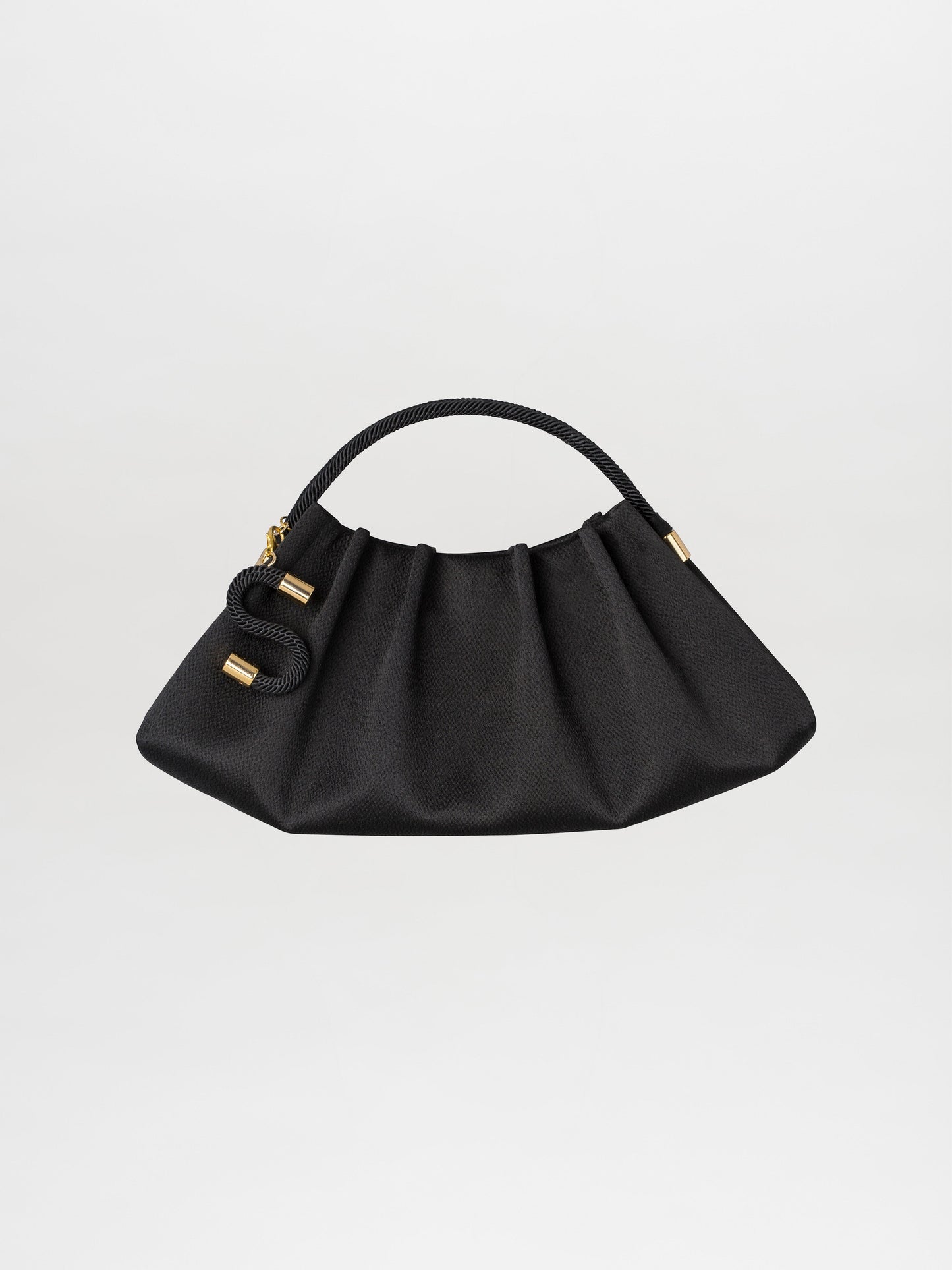 The Trapezius Clutch Black, a chic pleated handbag made from luxurious crepe fabric, showcases a curved handle and gold accents, elegantly displayed against a white background.