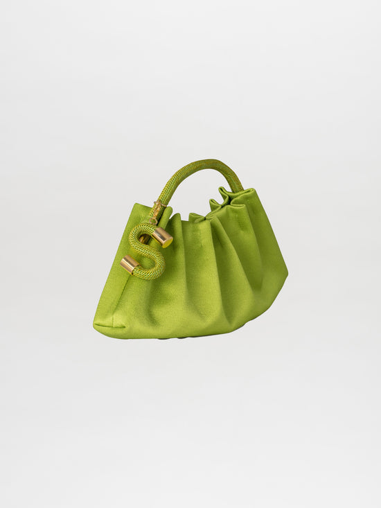 Introducing the Trapezius Clutch Lime: a pleated clutch crafted from crepe fabric, showcasing a vibrant green color and an organic, unique shape with a curved handle. It is elegantly adorned with gold accents and features a stylish S-shaped charm.