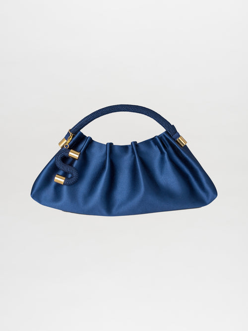 A satin navy Trapezius Clutch featuring a pleated design, gold accents, and a braided handle set against a plain background.