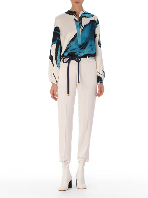 A white Triora Blouse Multi Abstract Waves with bold blue and black abstract print, featuring long sleeves and a V neckline with a tie.