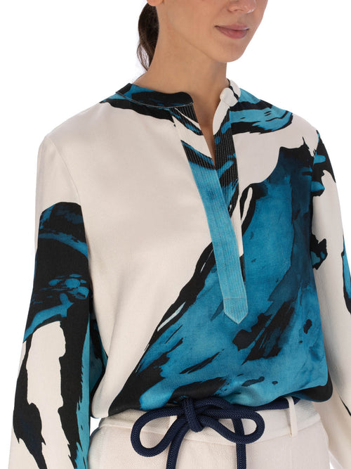 A white Triora Blouse Multi Abstract Waves with bold blue and black abstract print, featuring long sleeves and a V neckline with a tie.
