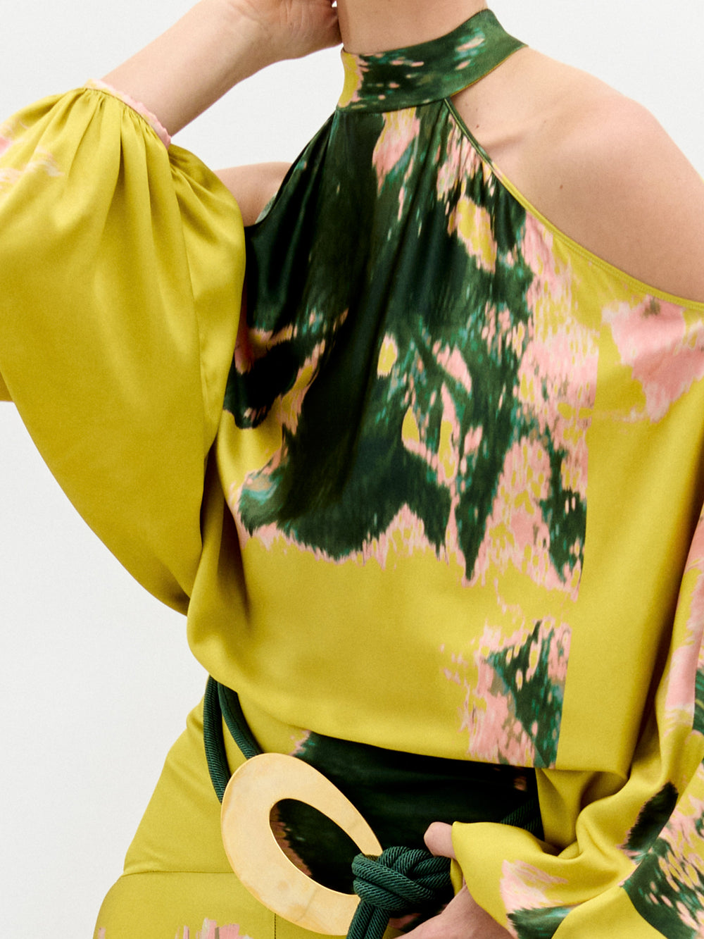 A person wears the Valeria Dress, a flowing maxi dress in yellow, pink, and green patterns with open shoulders and a 3D cord belt, standing against a plain white background.