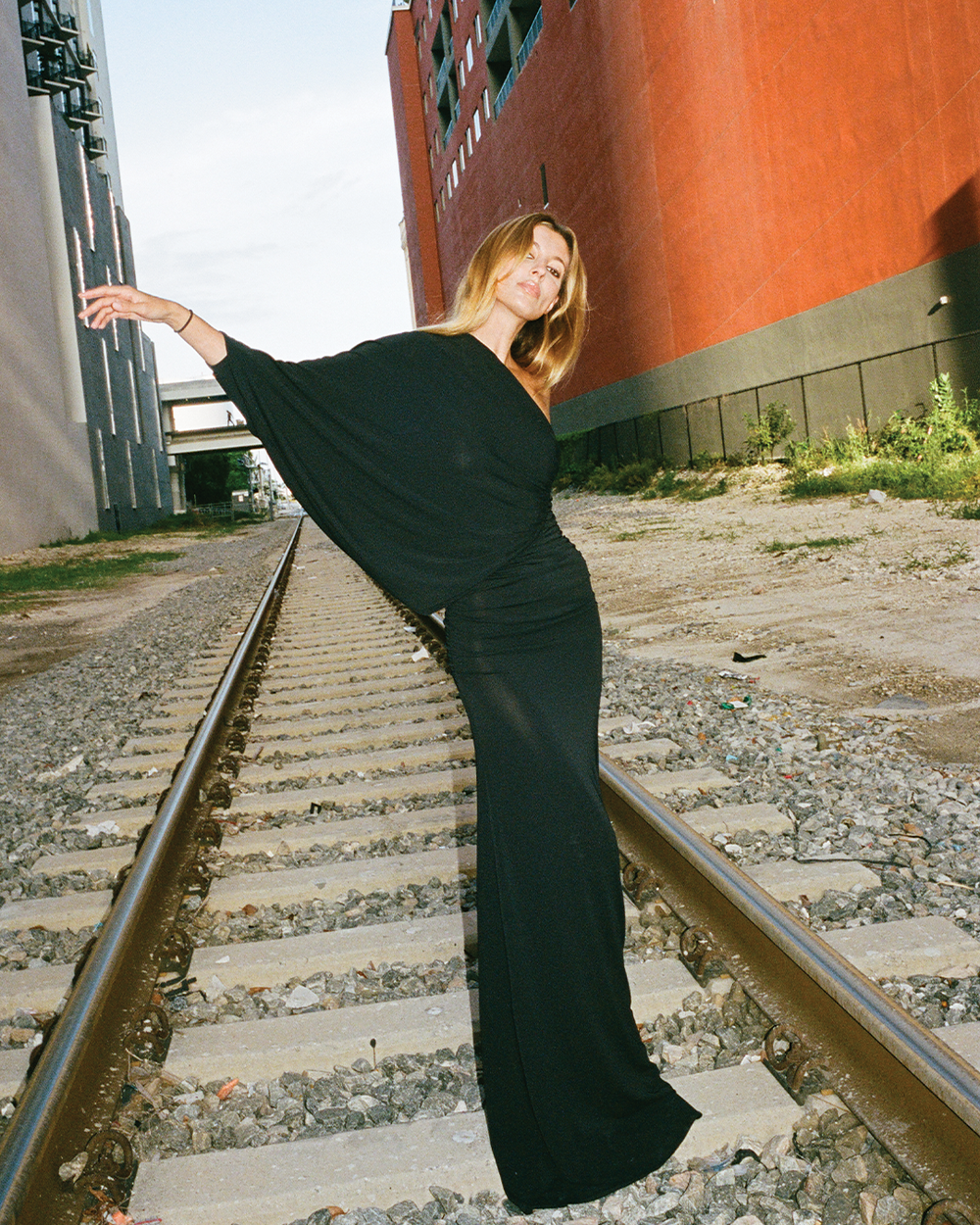 Woman in a black dress standing on train tracks with a red building in the background