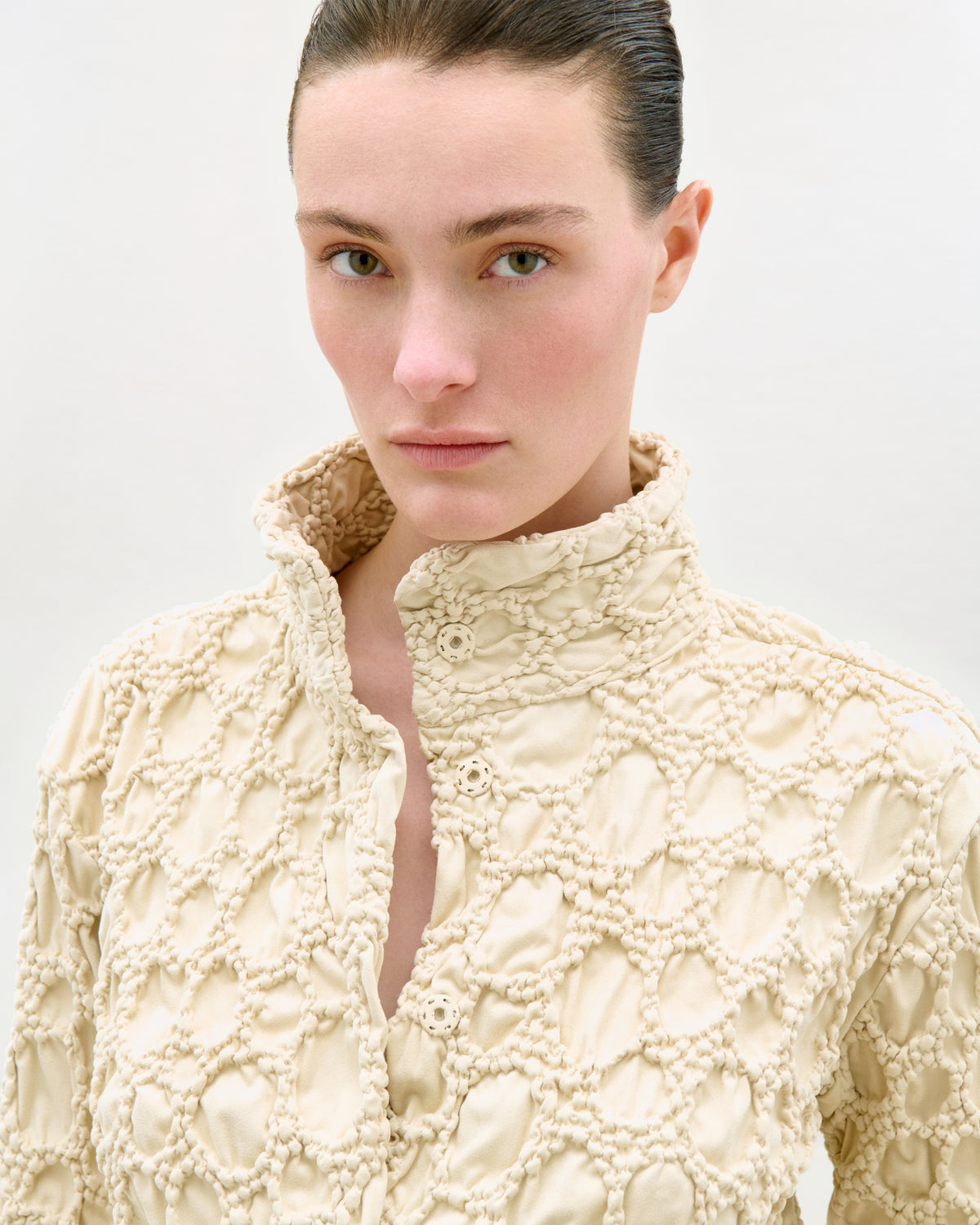 Woman wearing a textured cream-colored sweater against a plain background