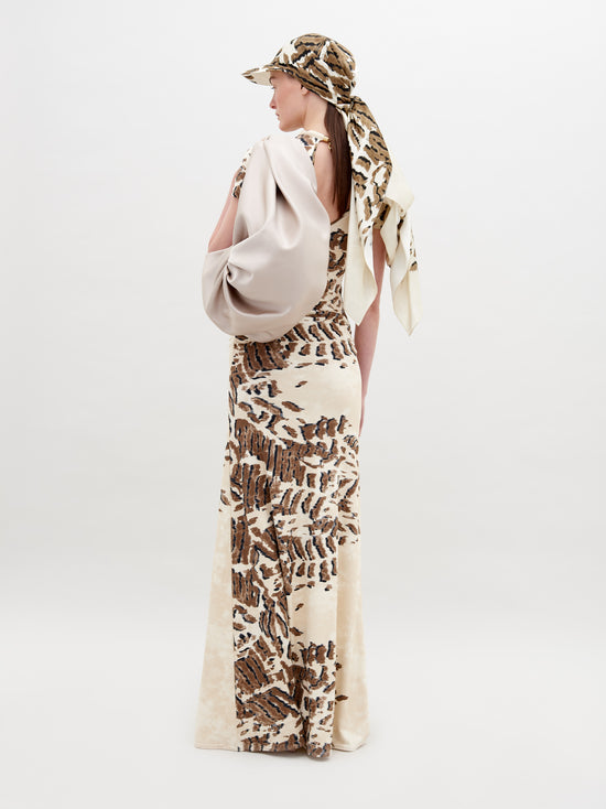 A person wearing a Yara Dress Beige Abstract Animal Print and cap with a white bag over their shoulder stands in front of a plain background, ready for pre-order by the November 15th, 2024 ship-by date.