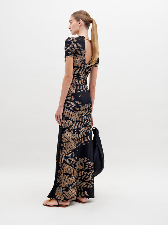 A woman stands against a plain white background wearing the Yara Dress Black Abstract Animal Print. She is holding a black bag and has her hair tied back in a low ponytail. Pre-order today for delivery by ship by date, November 15th, 2024.