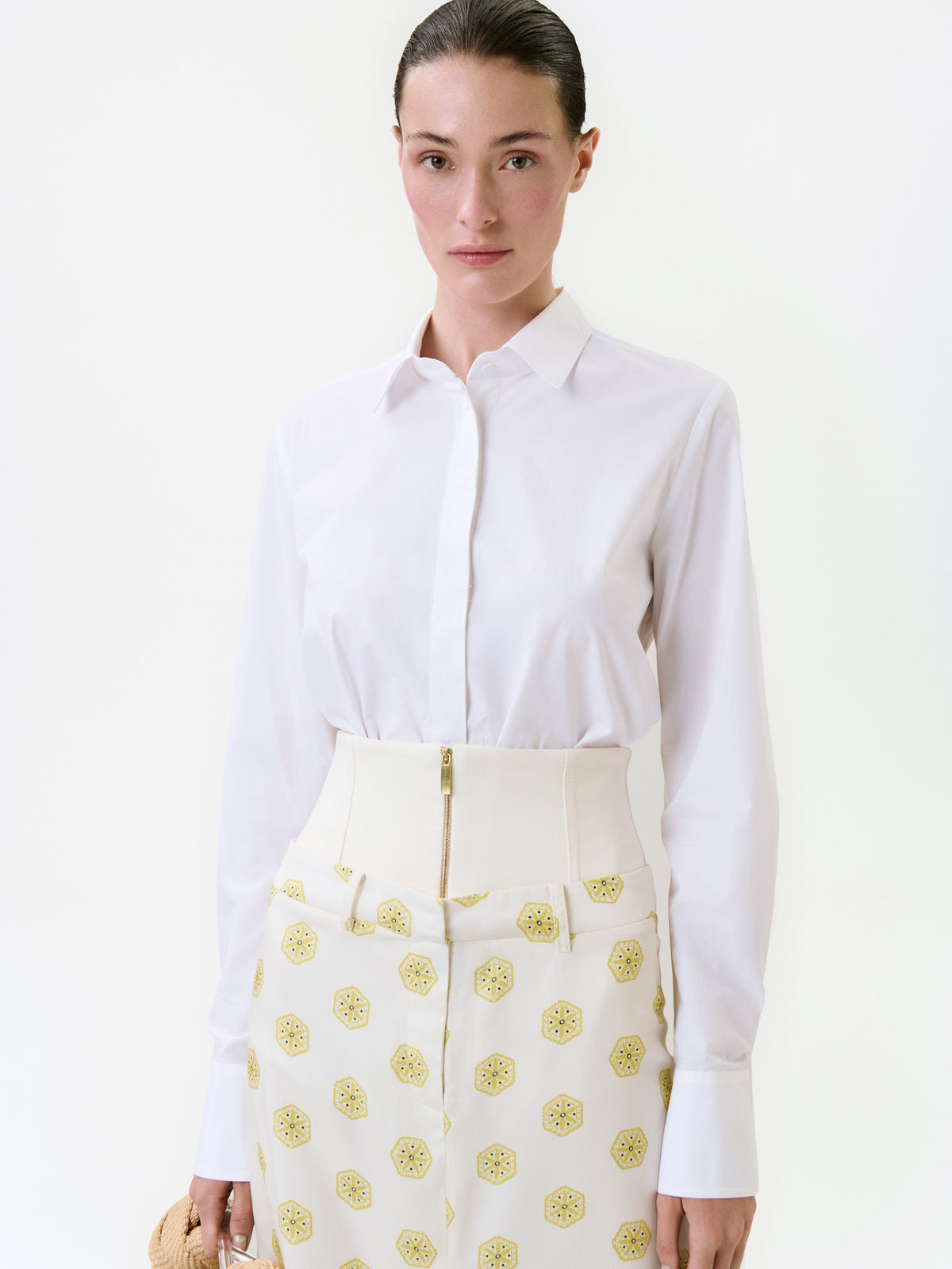 A person wearing a Yemi Shirt tucked into cream-colored trousers with a wide, zippered waistband and a repeating yellow geometric pattern.