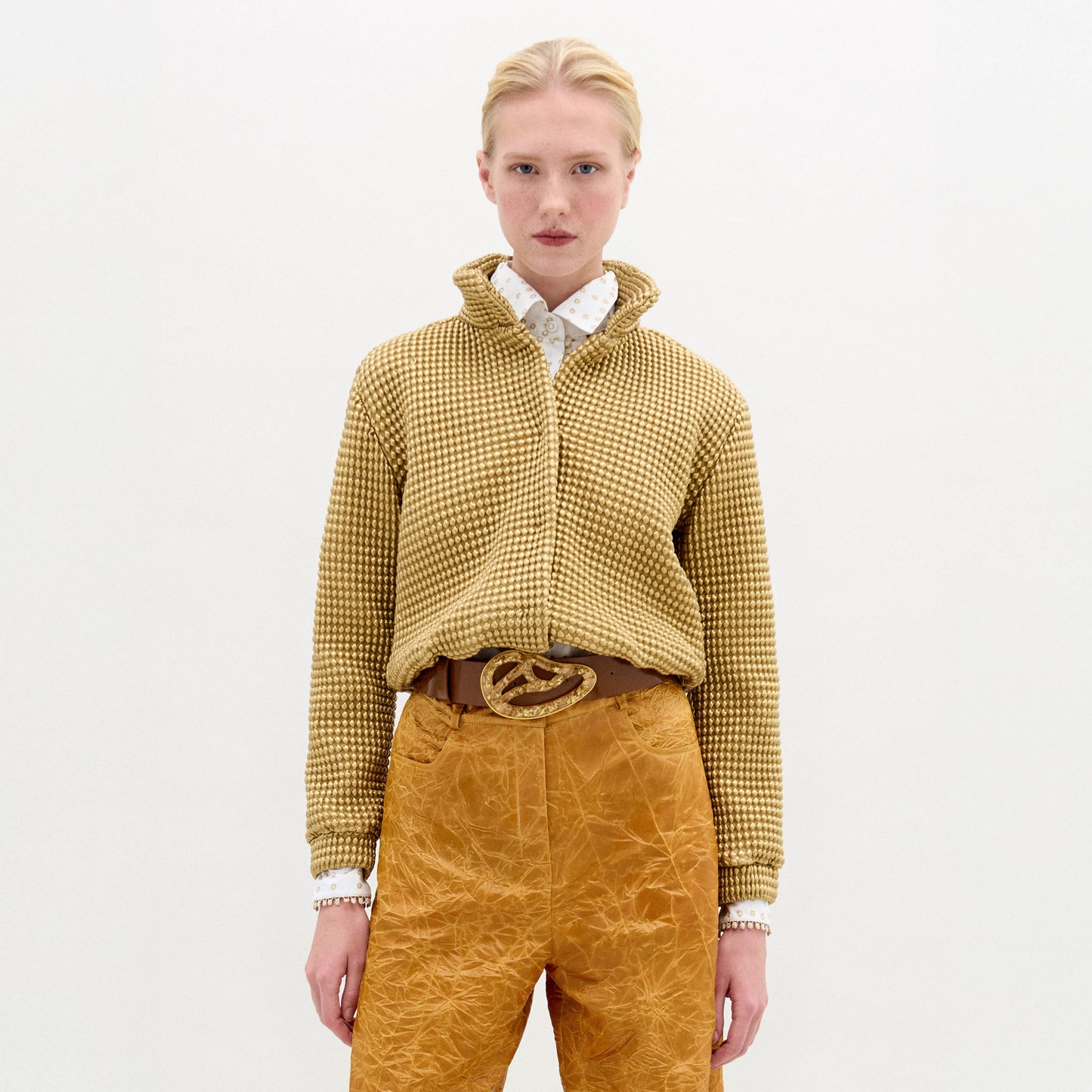 A woman wears the Zalta jacket, a brown sweater with an oversized fit, paired with gold pants.