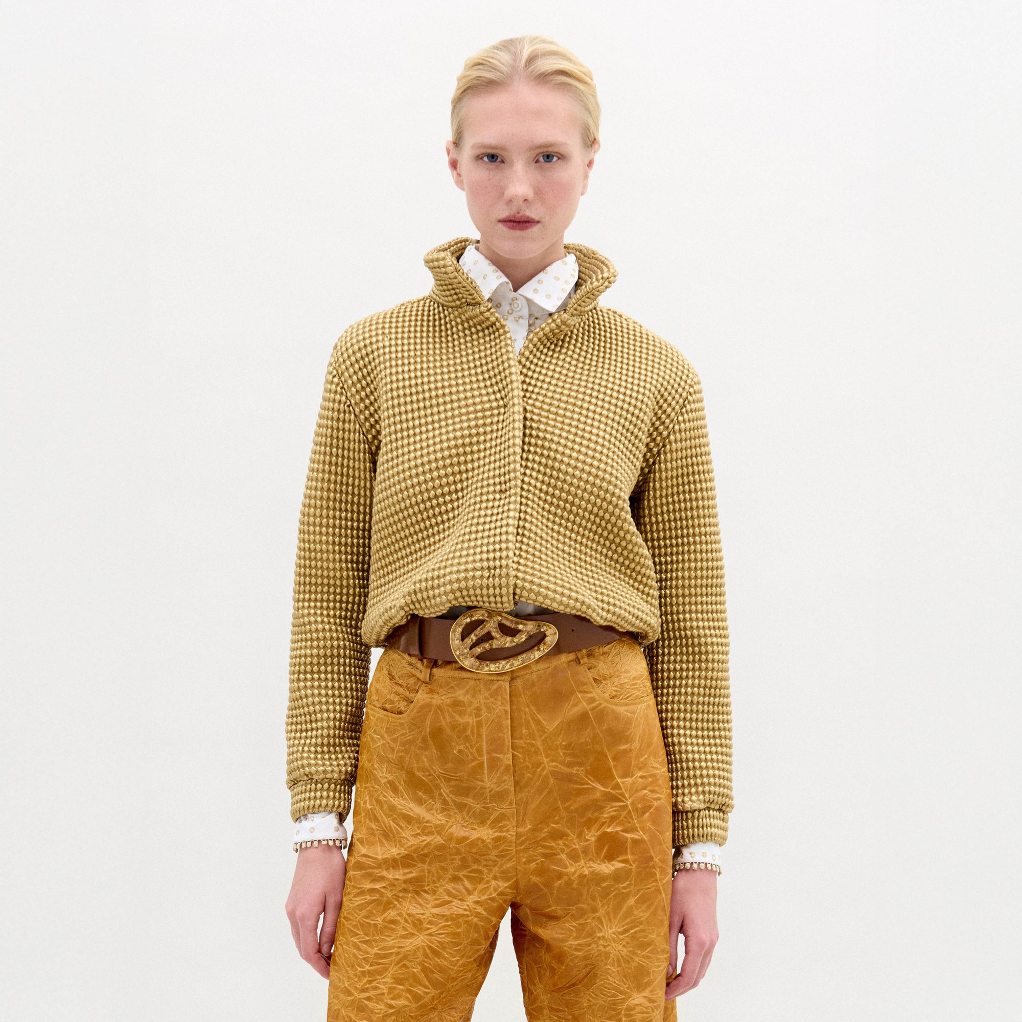 A woman wears the Zalta jacket, a brown sweater with an oversized fit, paired with gold pants.
