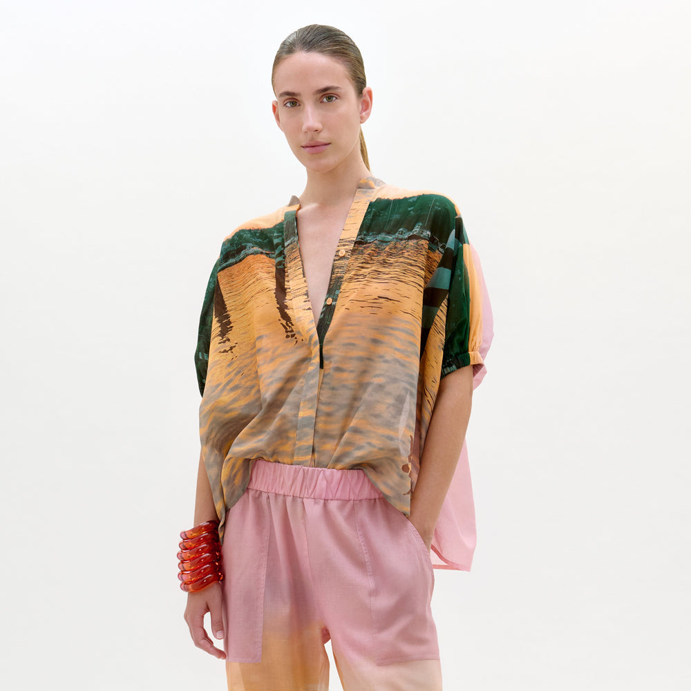 Model wearing a colorful top and pink pants on a white background