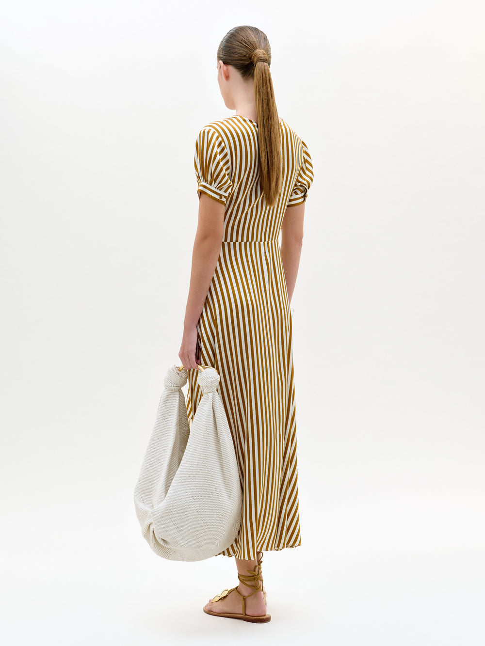 Woman in a striped dress holding a white bag on a white background