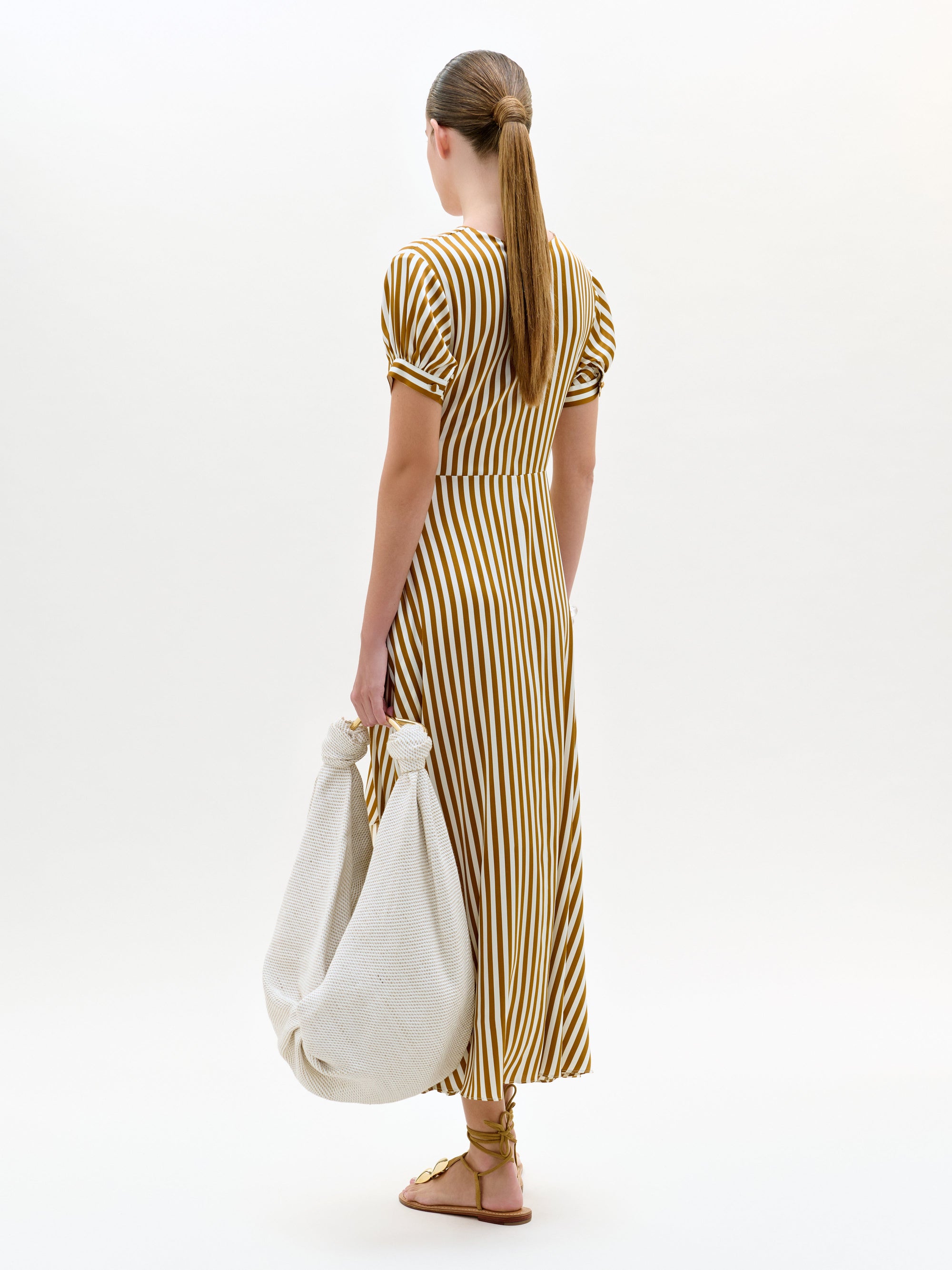 Woman in a striped dress holding a white bag on a white background