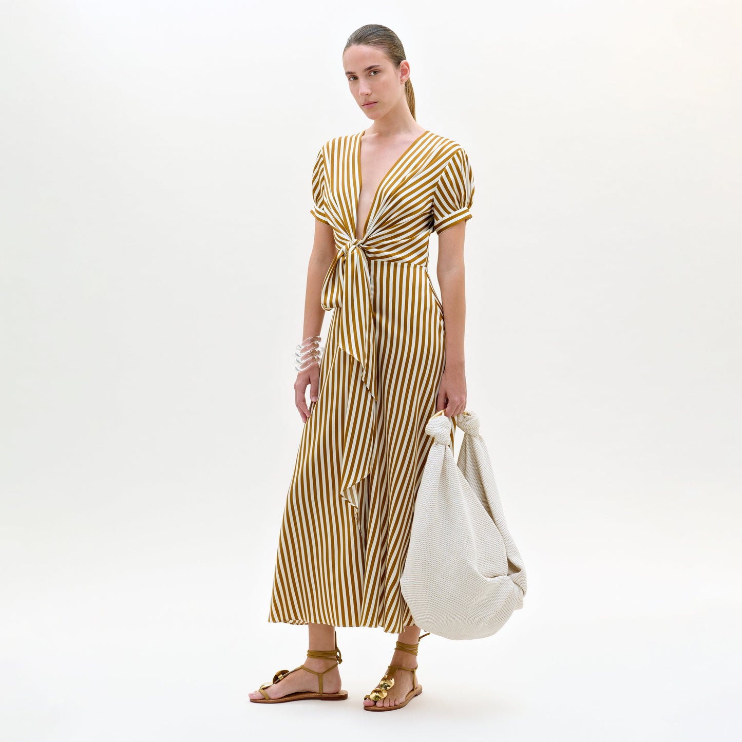 Woman wearing a yellow and white striped dress holding a white bag on a white background