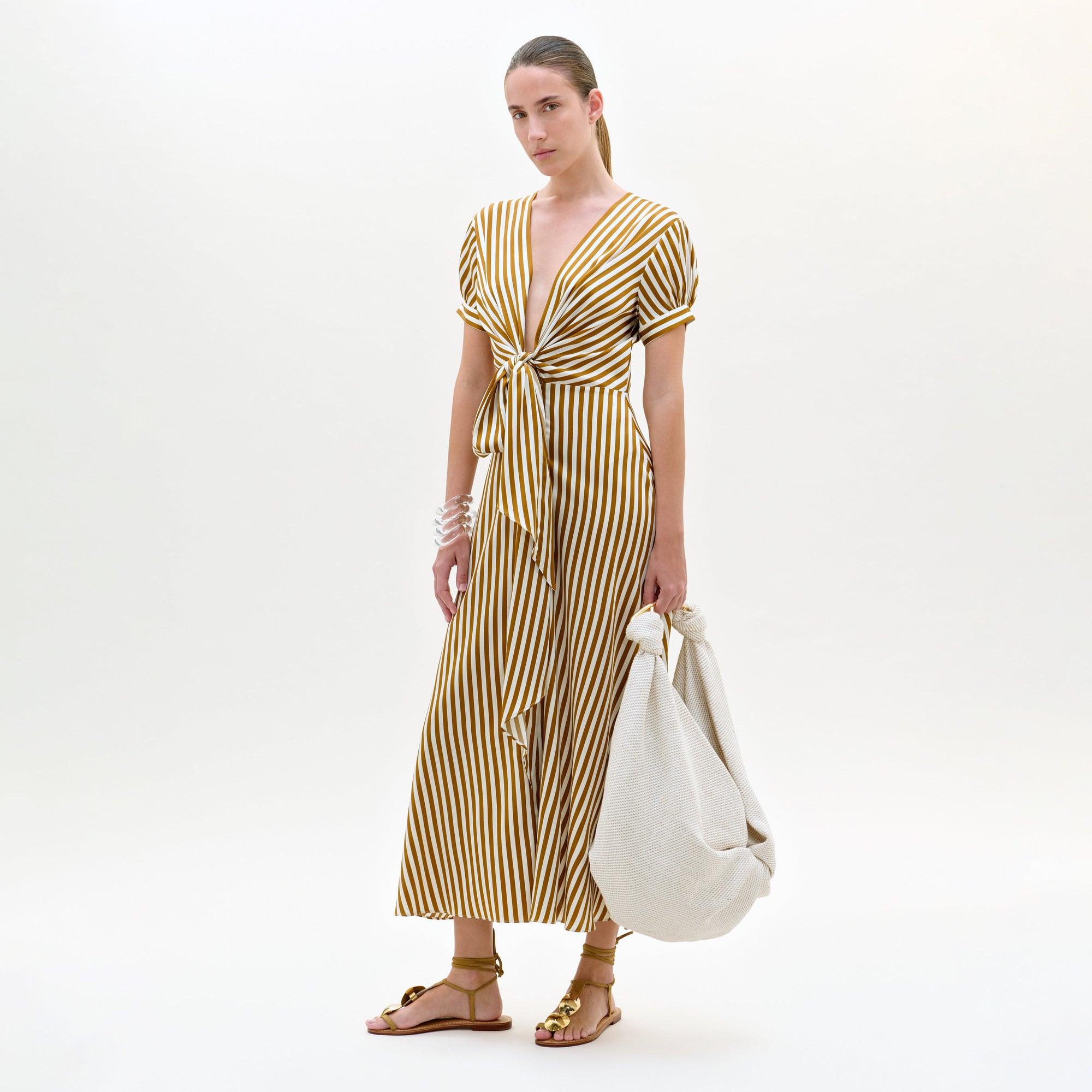 Woman wearing a yellow and white striped dress holding a white bag on a white background